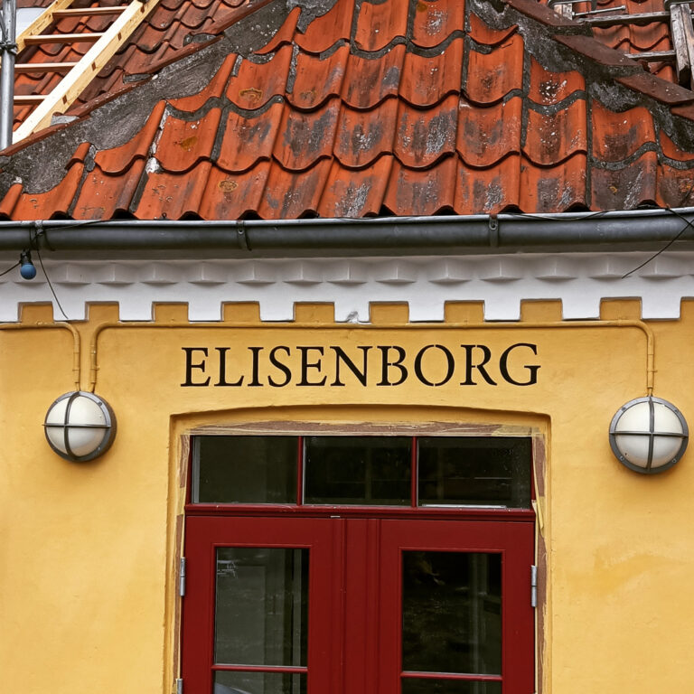 En rød hovedør i en gult hus, hvor der står Elisenborg over døren i sort