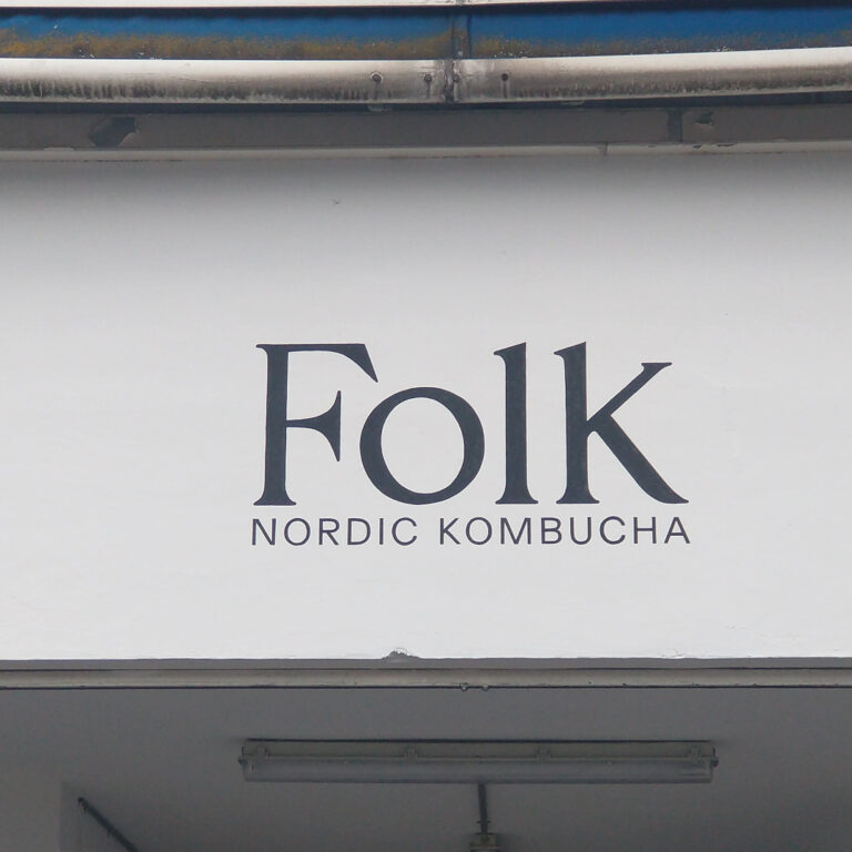 Et nærbillede at en hvid mur med teksten FOLK med stor bogstaver. Under Folk stor der Nordic Kombucha men store bogstaver dog er teksten en del mindre