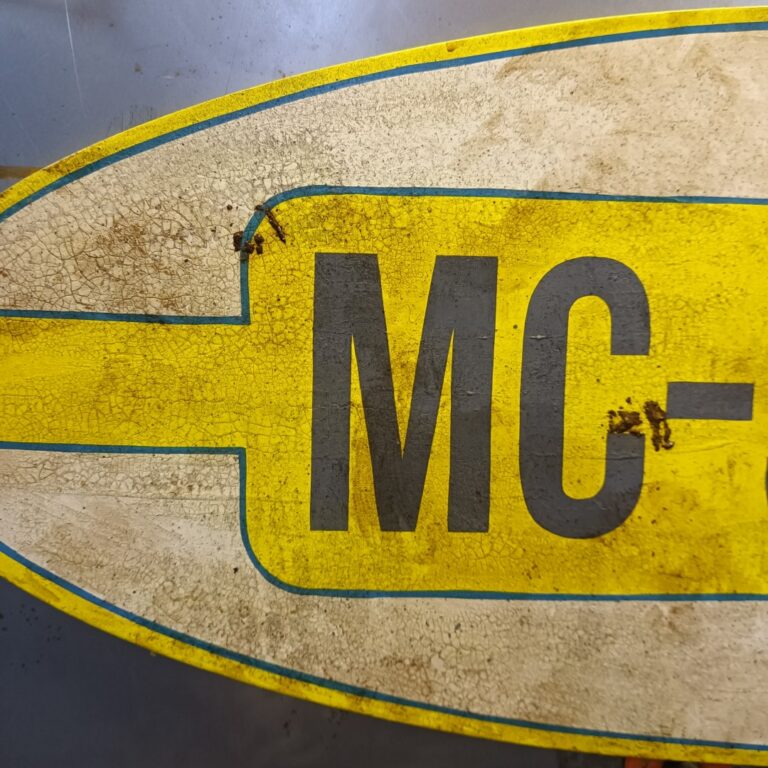 Nærbillede af guld, hvidt og blådt Mc-service skilt. Skiltet har en krakeleret baggrund, og skiltet ser snavset ud.