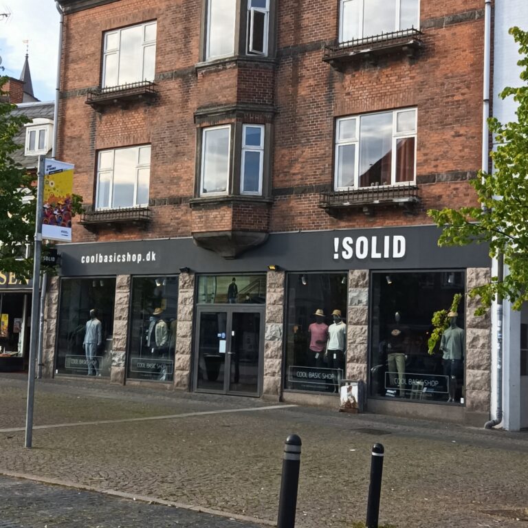 Håndmalet facadetekst på ændre bygning i Ahlgade i Holbæk. Bundfarven er koksgrå og teksten er skrevet med hvid farve. På teksten står der !Solid.