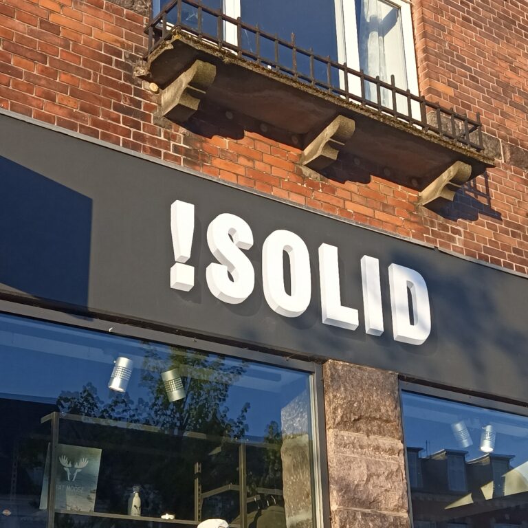 En grå facade over butiksvinduer hvor der står SOLID med hvide bogstaver i en 3D effekt