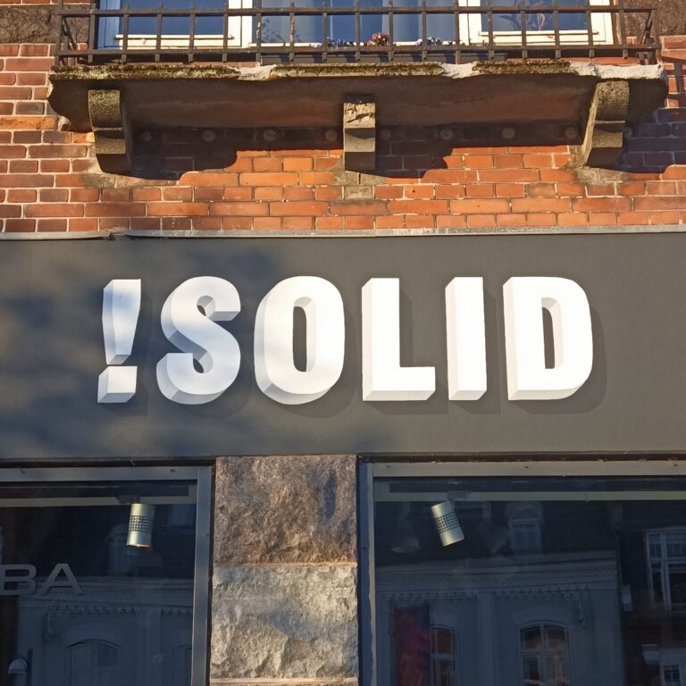 En grå facade over butiksvinduer hvor der står SOLID med hvide bogstaver i en 3D effekt